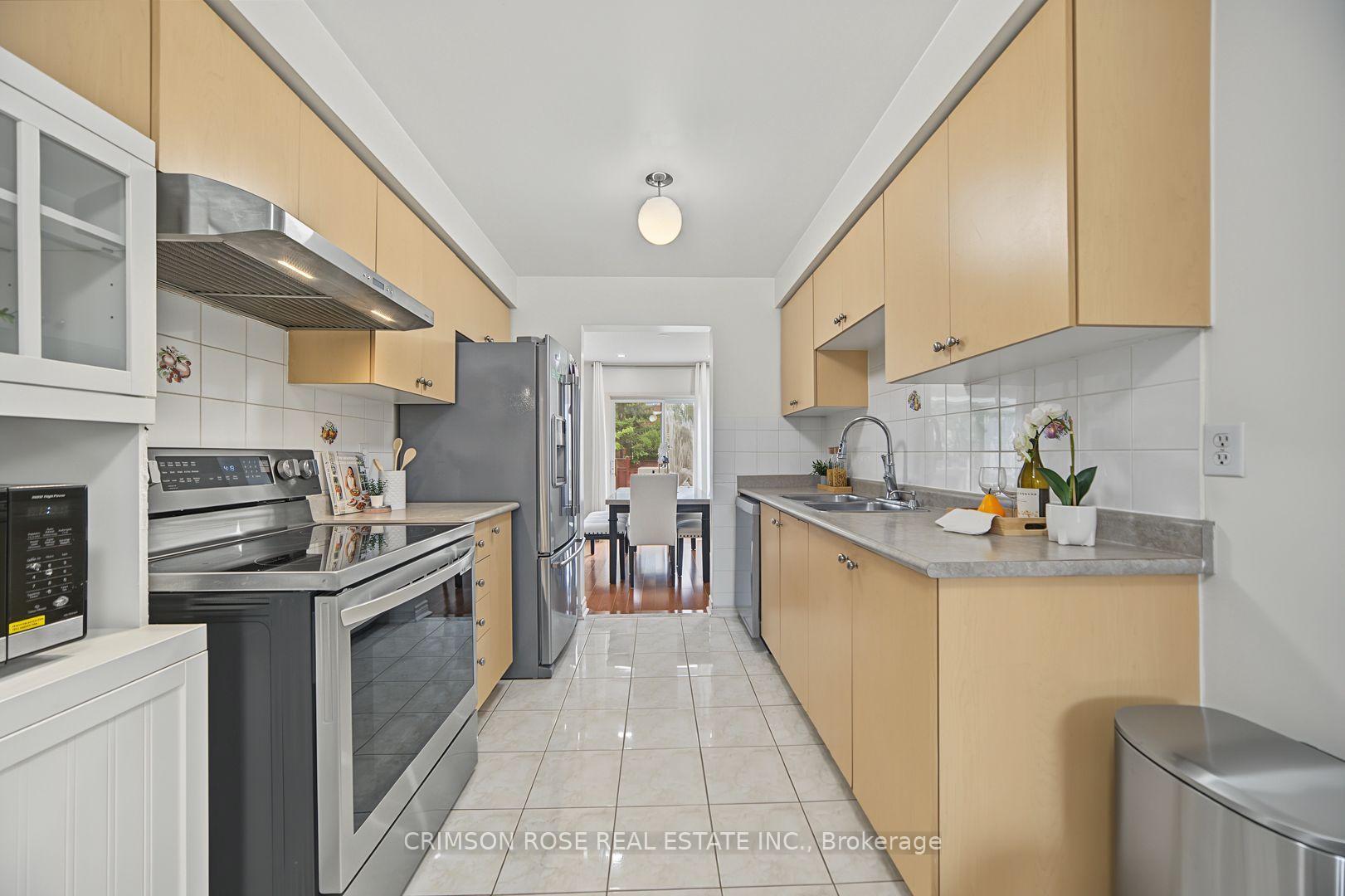 Galley kitchen with light wood cabinets, stainless-steel appliances, and a dining area beyond.