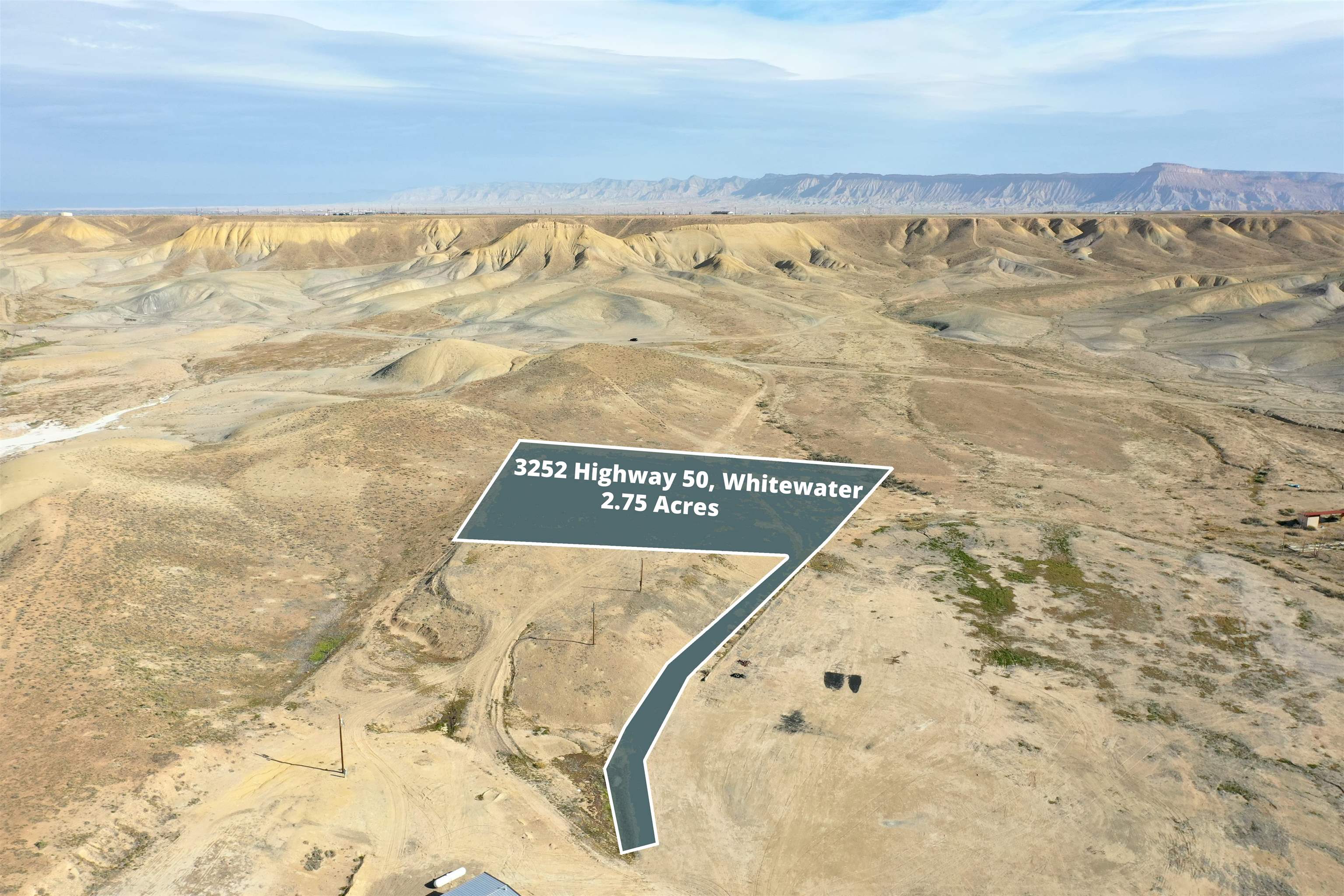 Aerial view of vacant 2.75-acre desert parcel outlined against eroded hills and distant mesas.