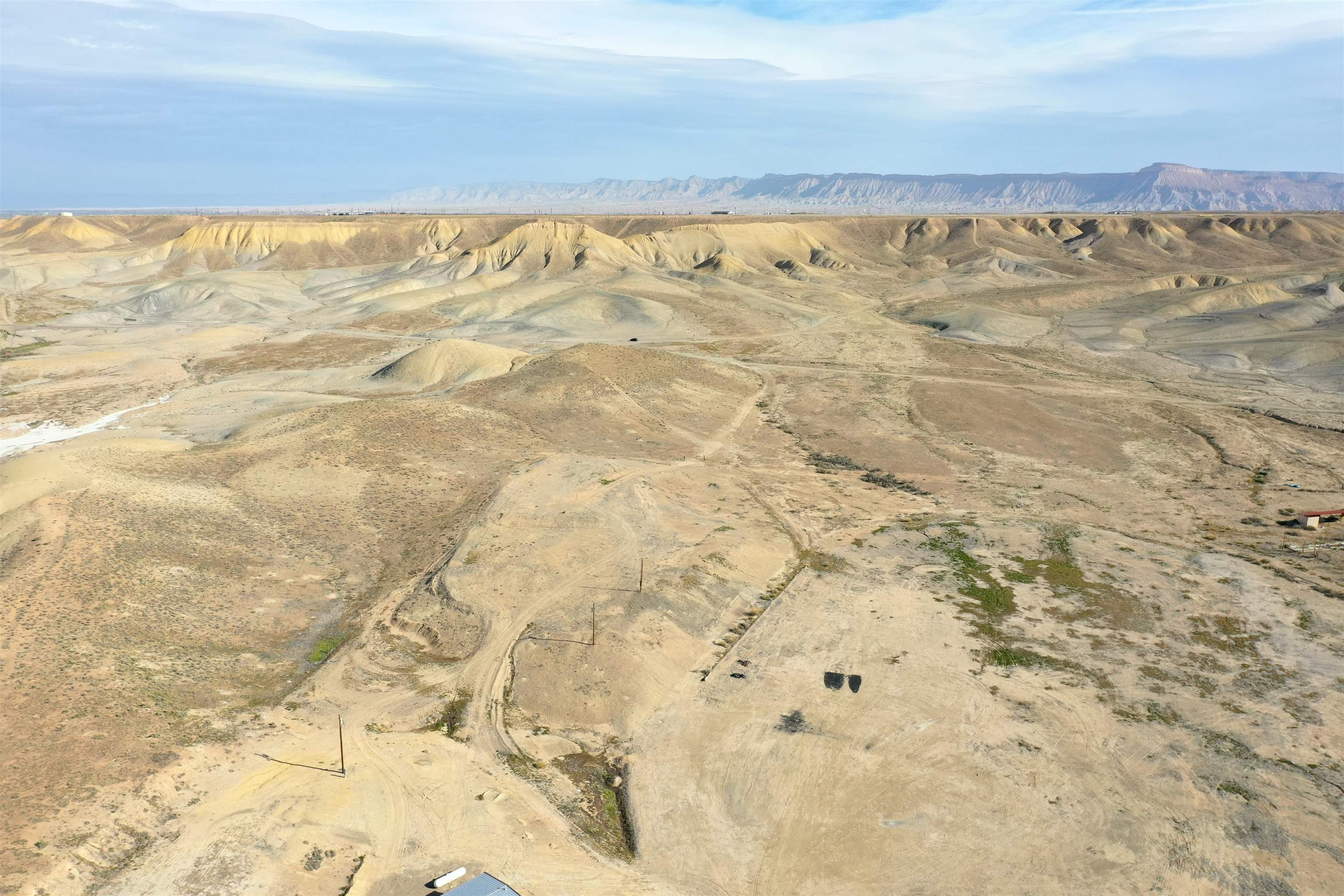 Aerial view of dry rolling land with dirt tracks and distant mesas.