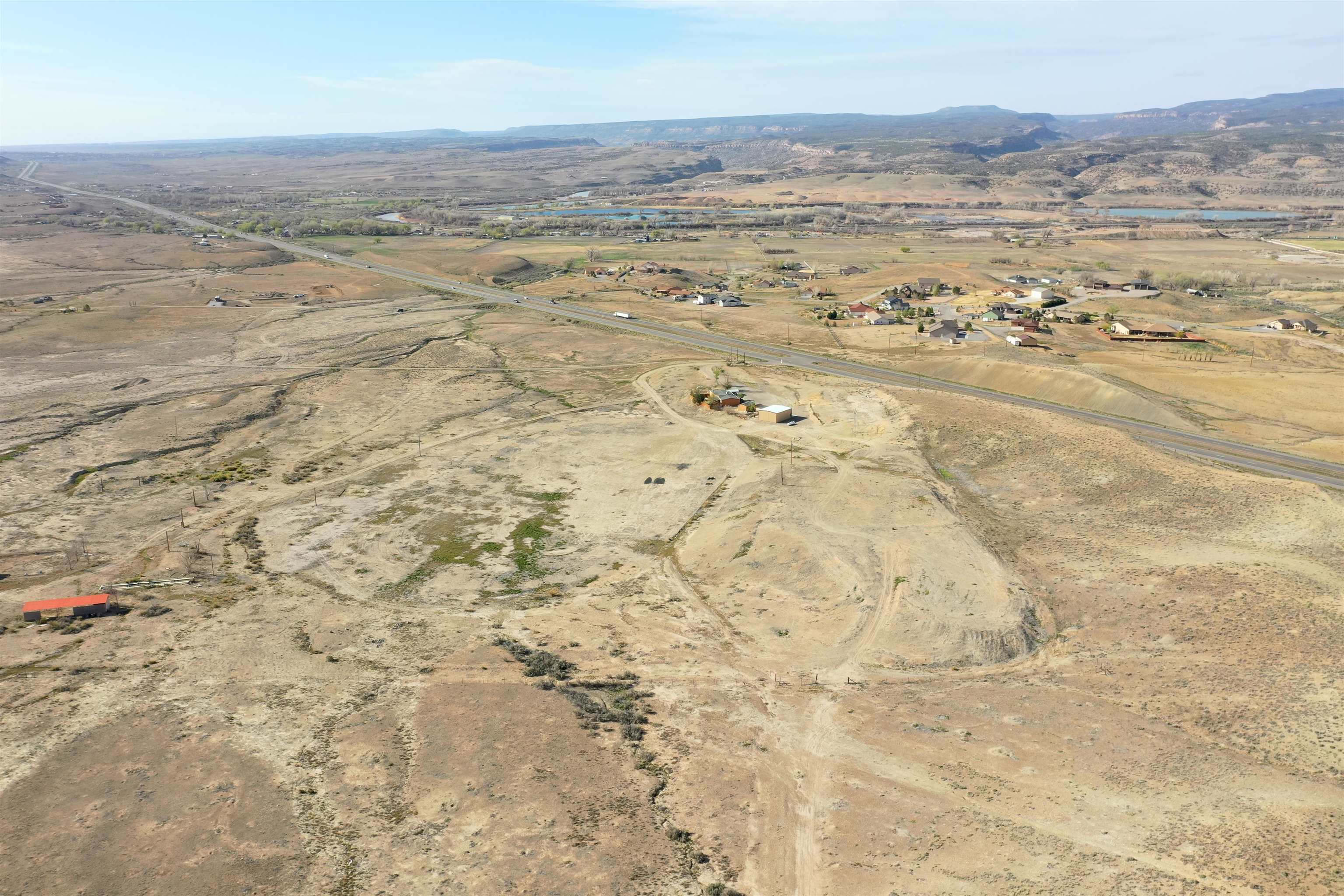 Aerial view of a bare rural parcel beside Highway 50, with distant homes, river, and mesas.
