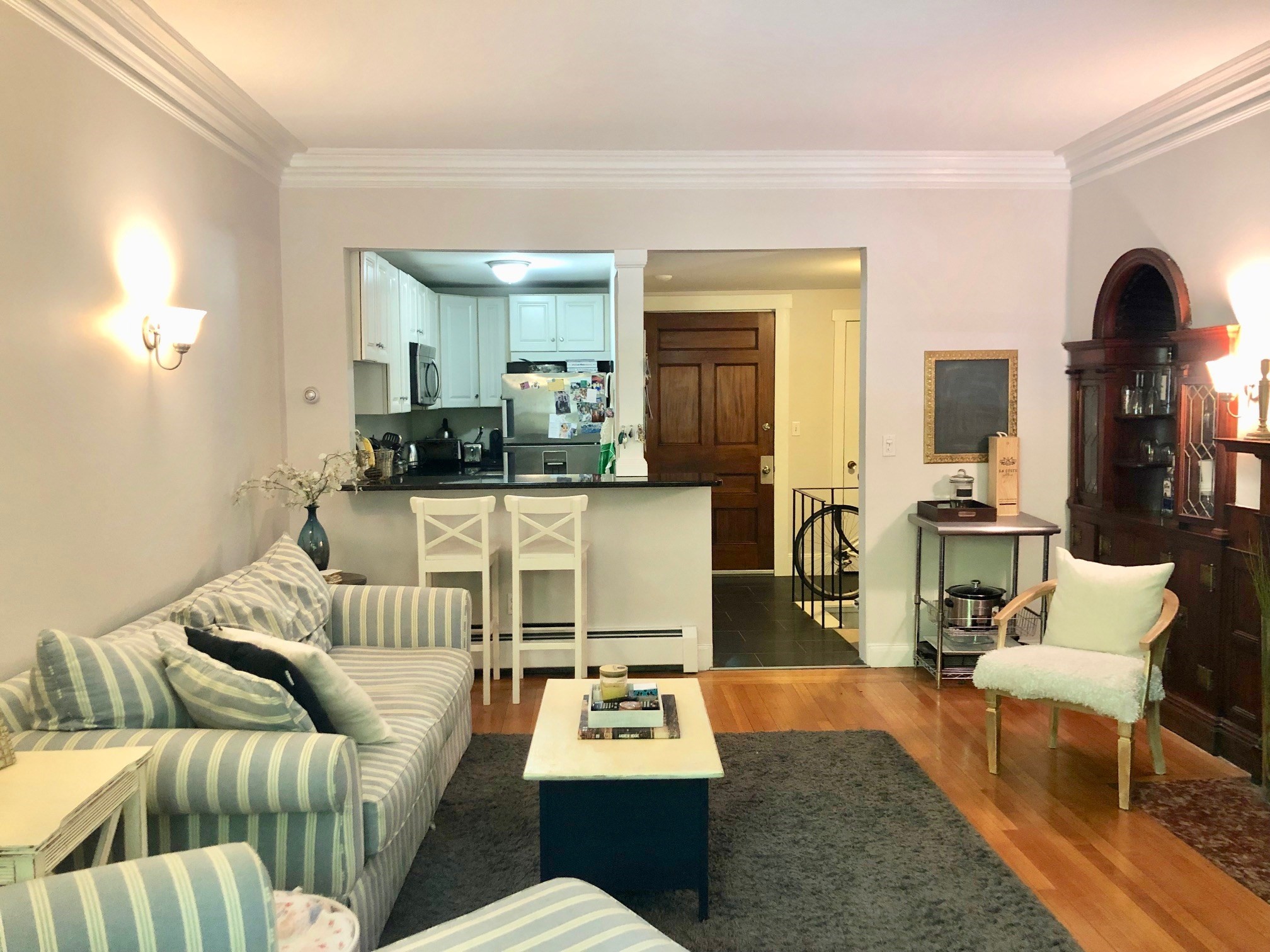 Living room with a striped sofa, hardwood floors, and an open kitchen.