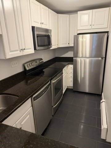 Compact kitchen with white cabinets, dark countertops, and stainless steel appliances.