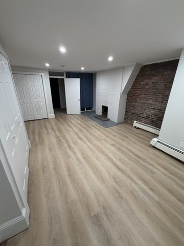 Unfurnished room with light wood floors, a brick accent wall, and a small fireplace.