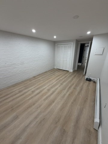 Room with light wood-look flooring, a white brick wall, and a closet beside an open doorway.