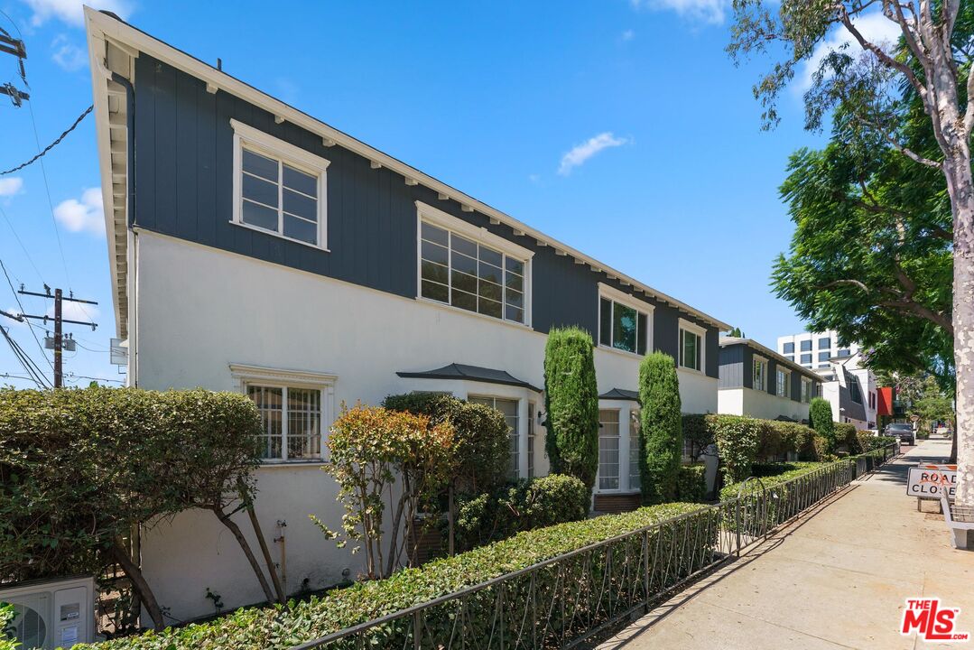Two-story white and dark blue building with landscaped frontage and a metal fence along the sidewalk.