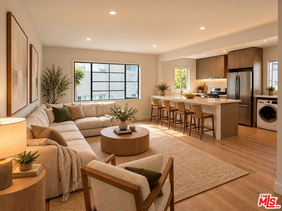 Open-plan living room and kitchen with a beige sectional, large black-framed window, and wood-cabinet island.