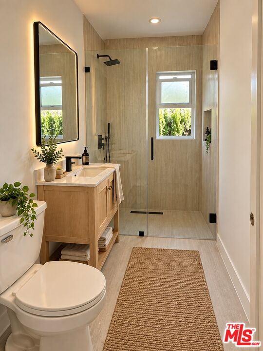 Bathroom with a glass-enclosed shower, light wood vanity, and window overlooking greenery.