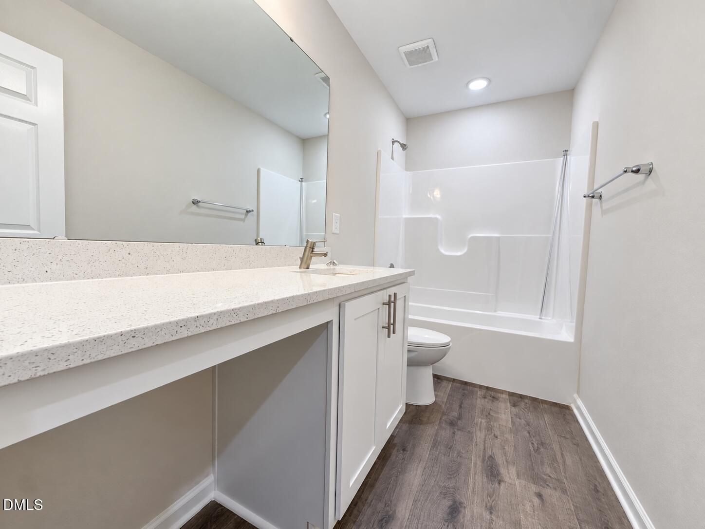 Bathroom with a long speckled vanity, large mirror, and white tub-shower enclosure.