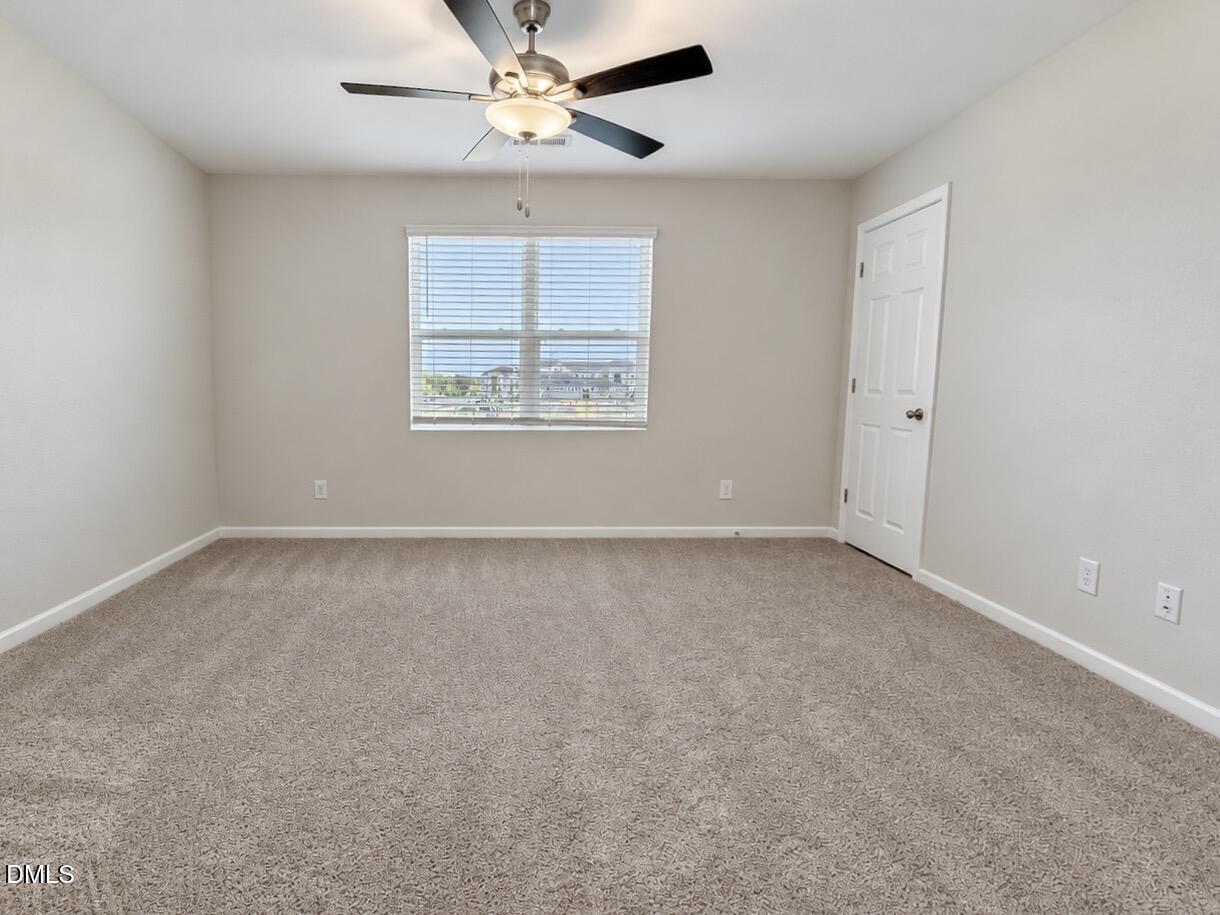 Empty carpeted bedroom with a ceiling fan and a window with blinds.