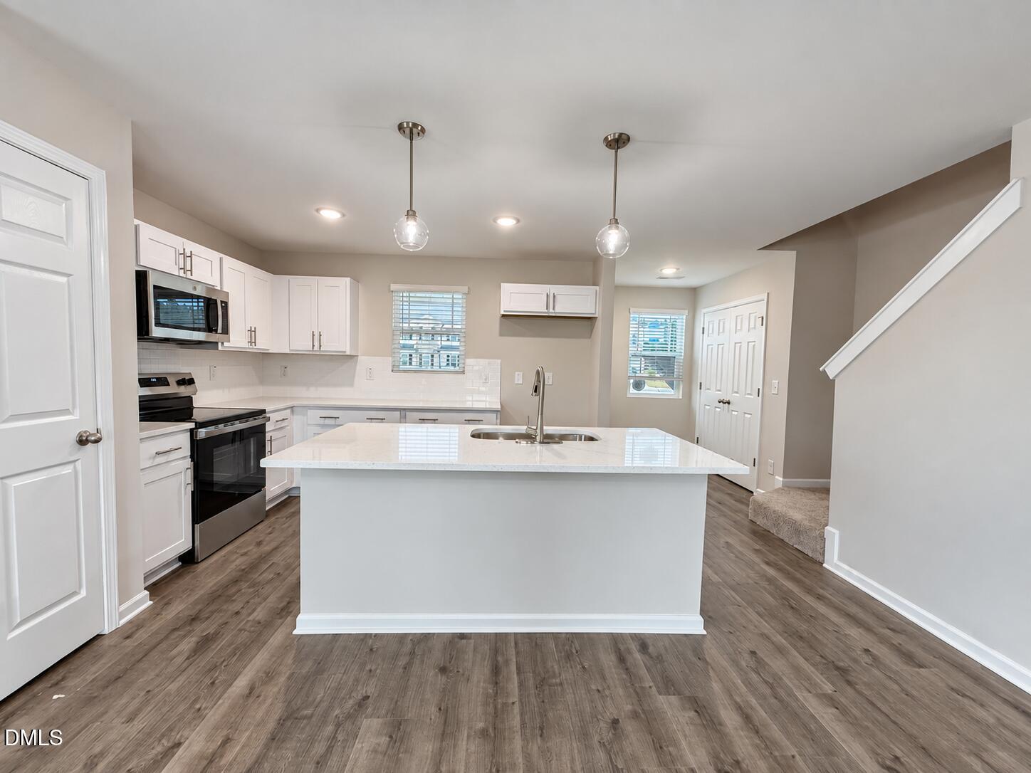 Kitchen with white cabinetry, stainless steel appliances, and a large island with a double-basin sink.