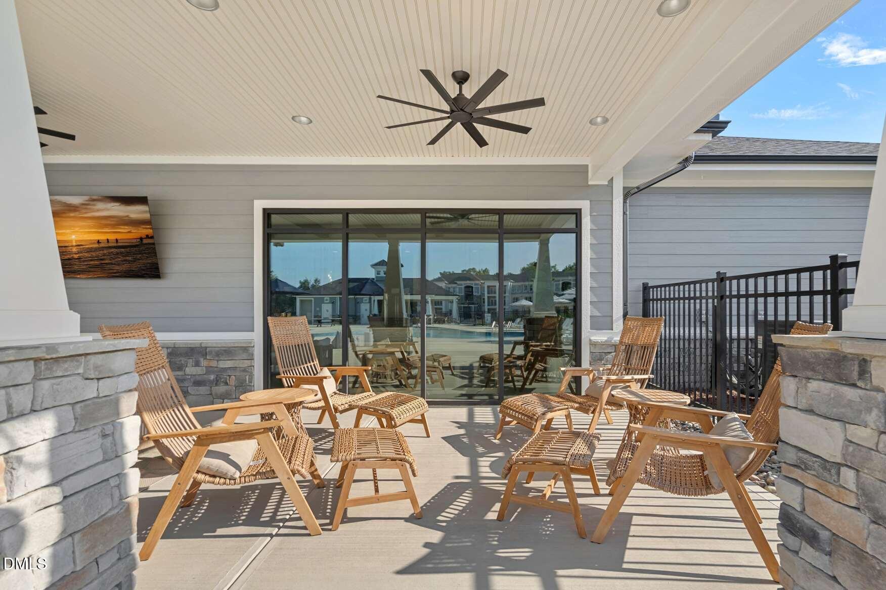 Covered patio with woven lounge chairs, a large ceiling fan, and sliding glass doors.