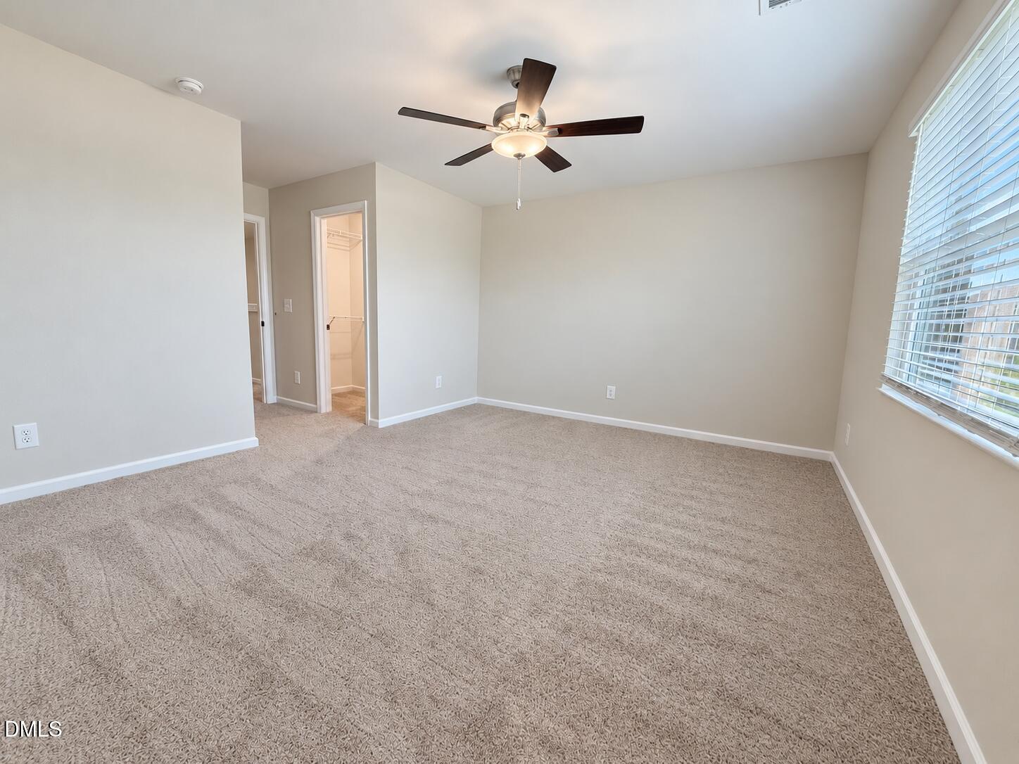 Empty carpeted bedroom with a ceiling fan, window blinds, and an open closet doorway.