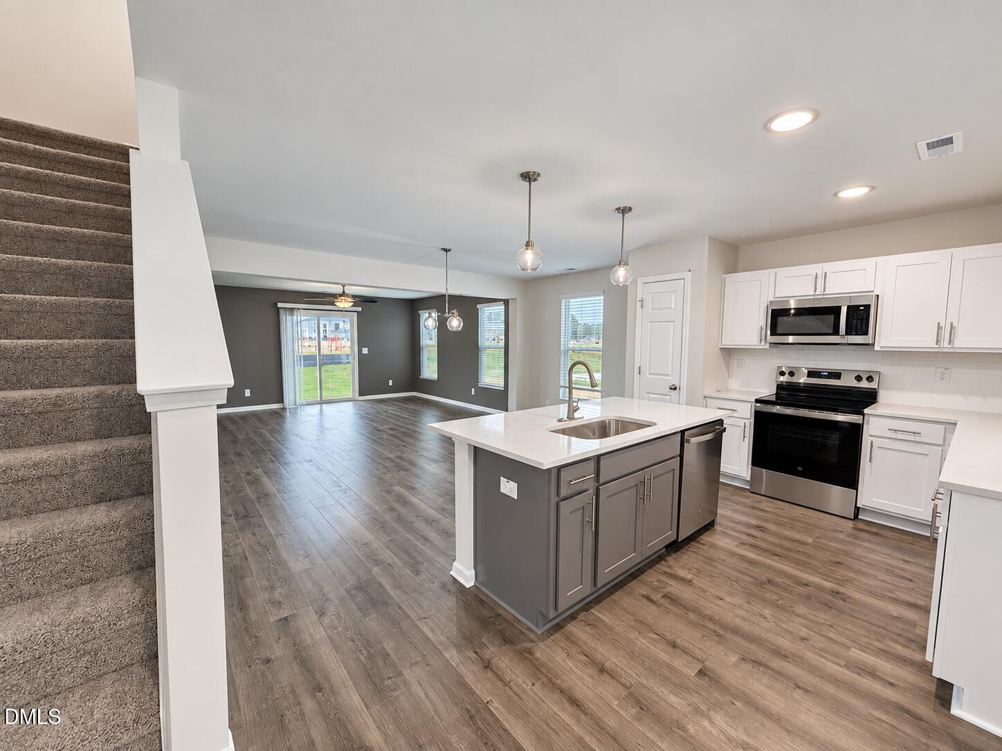 Open-plan kitchen and living area with a gray island, stainless steel appliances, and carpeted stairs.