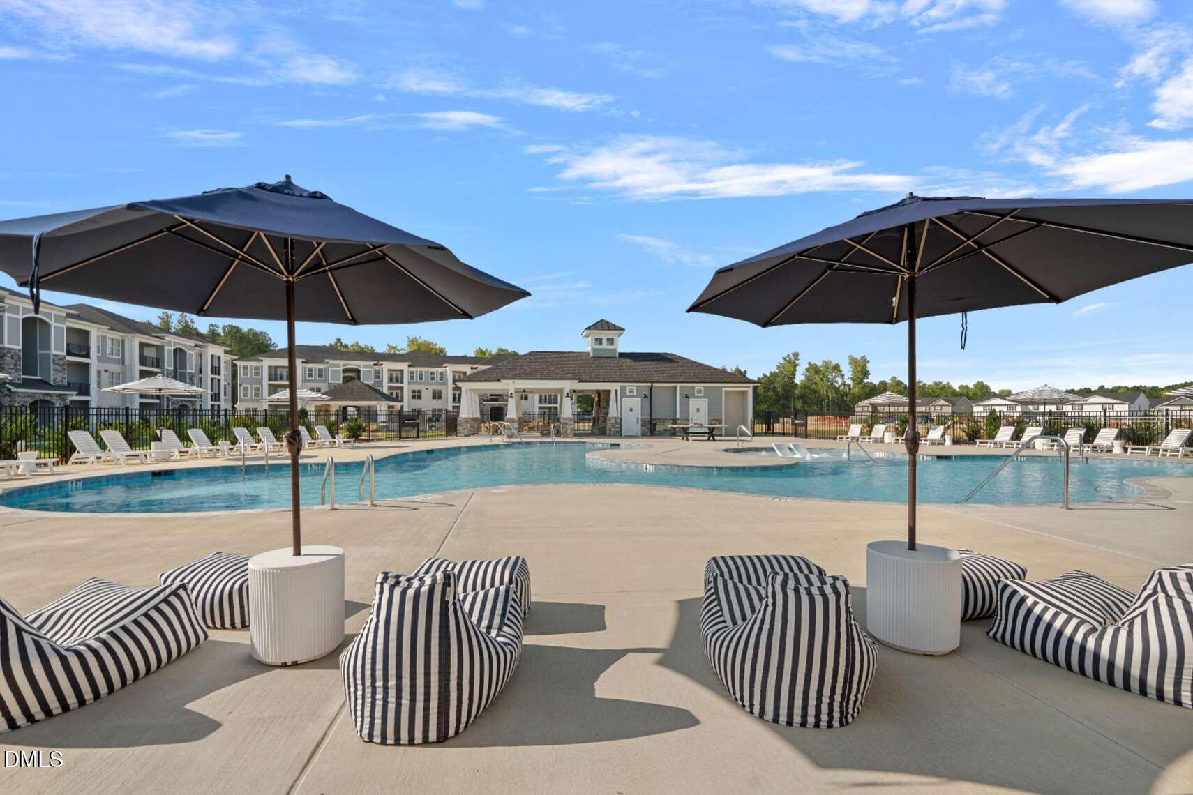 Community pool with black umbrellas and striped lounge seating, apartment buildings and clubhouse behind it.