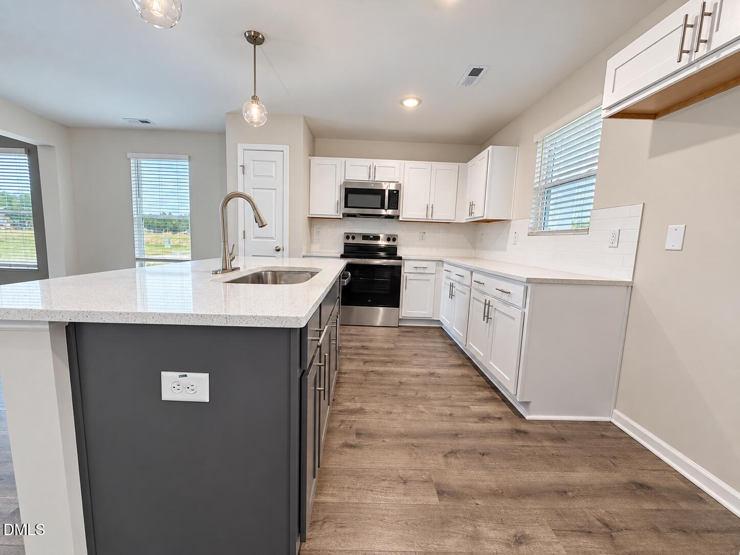 Bright kitchen with white cabinetry, gray island, stainless appliances, and wood-look flooring.