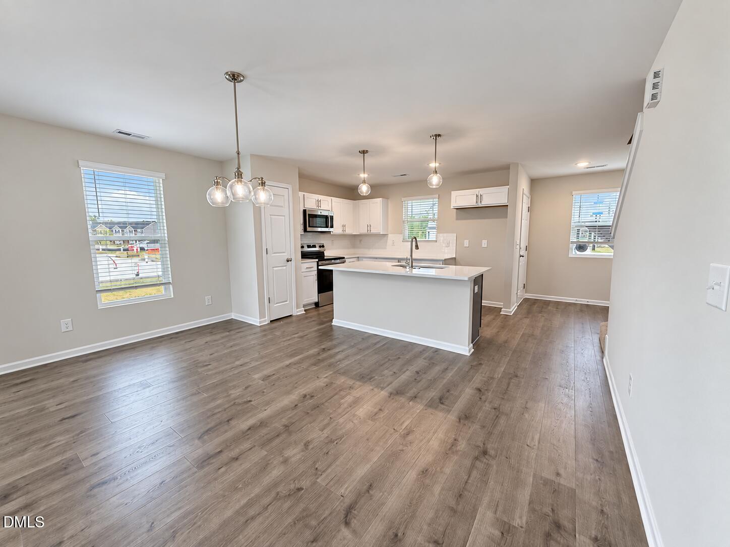 Open-plan kitchen with white cabinets, stainless steel appliances, and a sink peninsula beside an empty dining area.