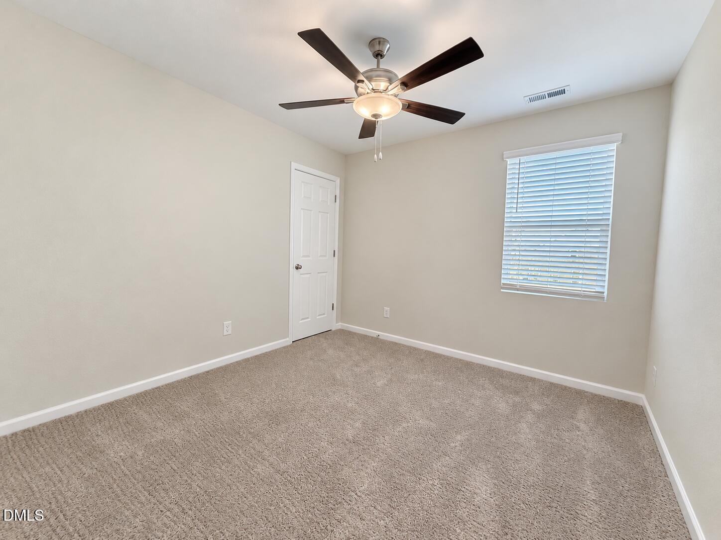 Empty carpeted bedroom with a dark ceiling fan and a window with white blinds.