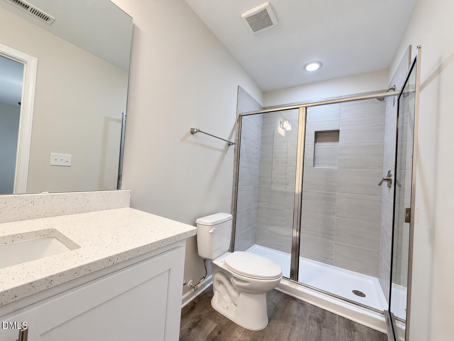 Bathroom with a tiled glass shower, recessed niche, white vanity, and dark wood-look flooring.