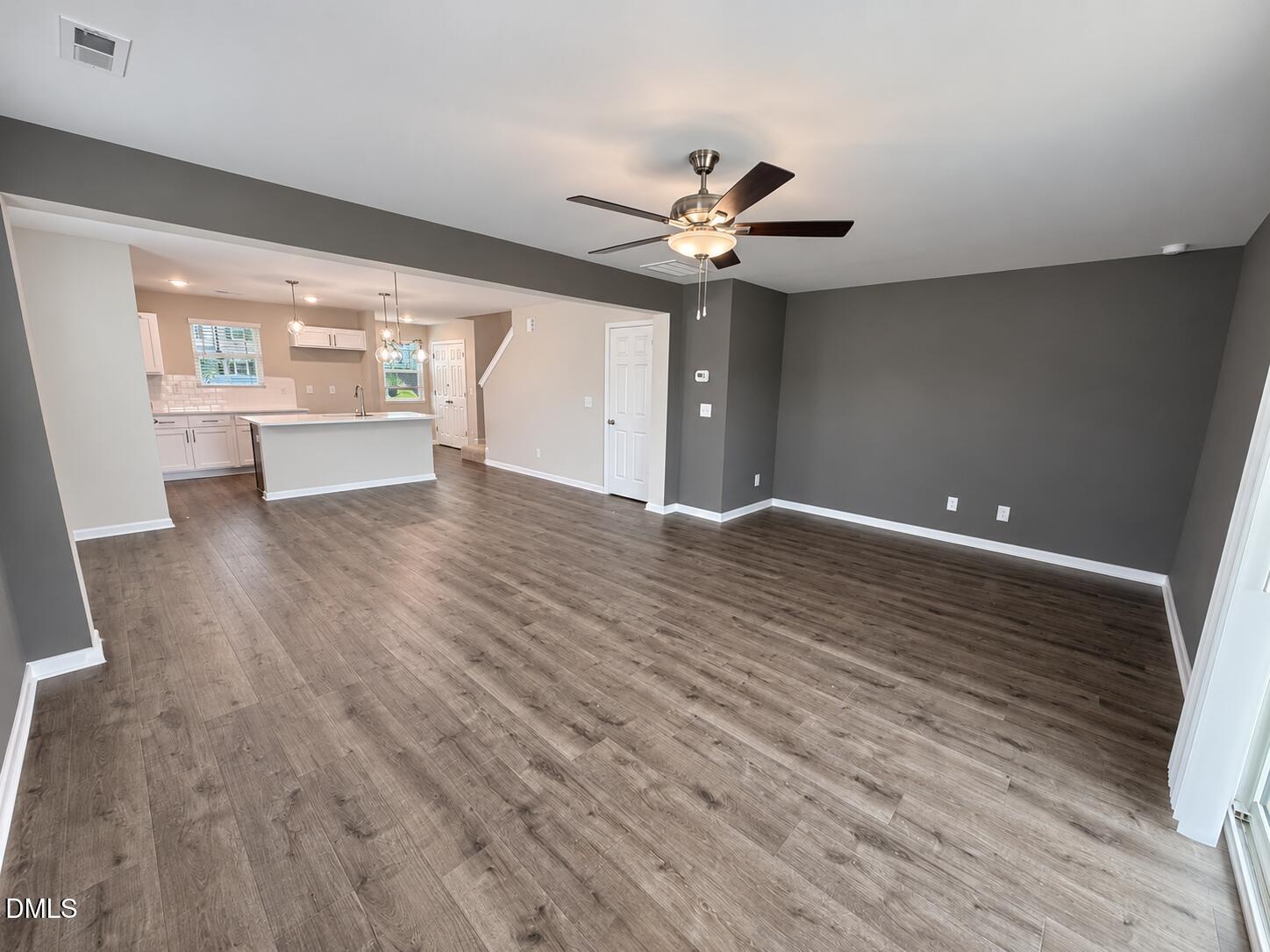Vacant open-plan living room with wood-look floors, gray accent wall, ceiling fan, and kitchen peninsula.
