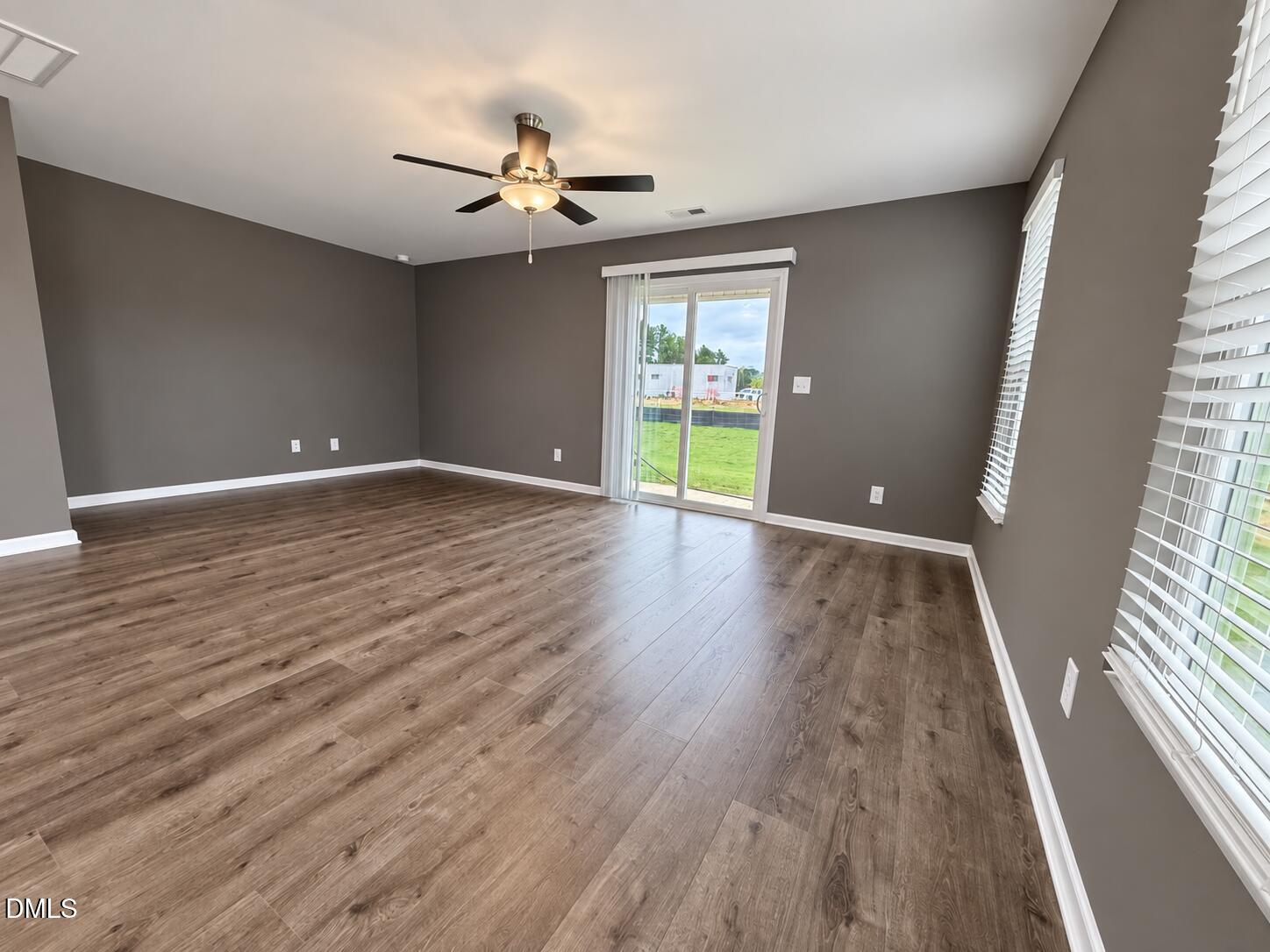 Vacant living room with wood-look flooring, a ceiling fan, and sliding glass doors to the yard.