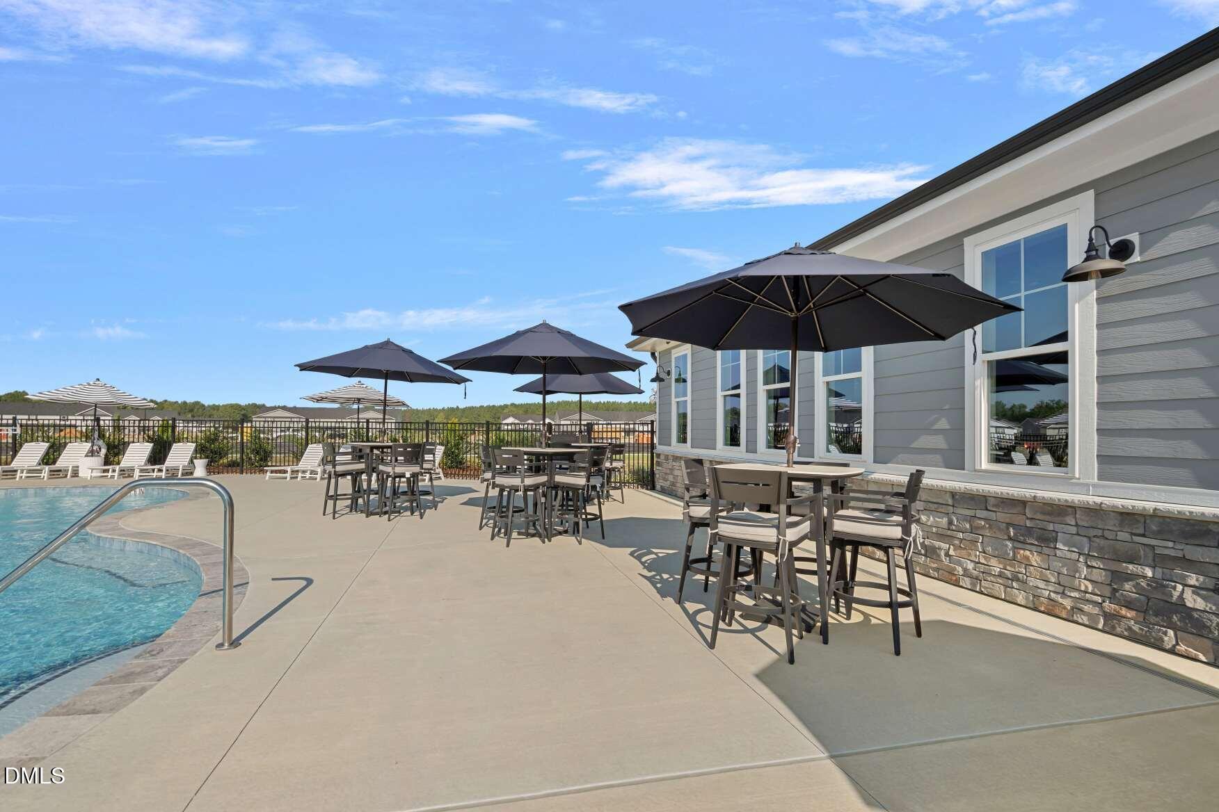 Outdoor pool beside a gray building, with shaded tables and lounge chairs on the deck.