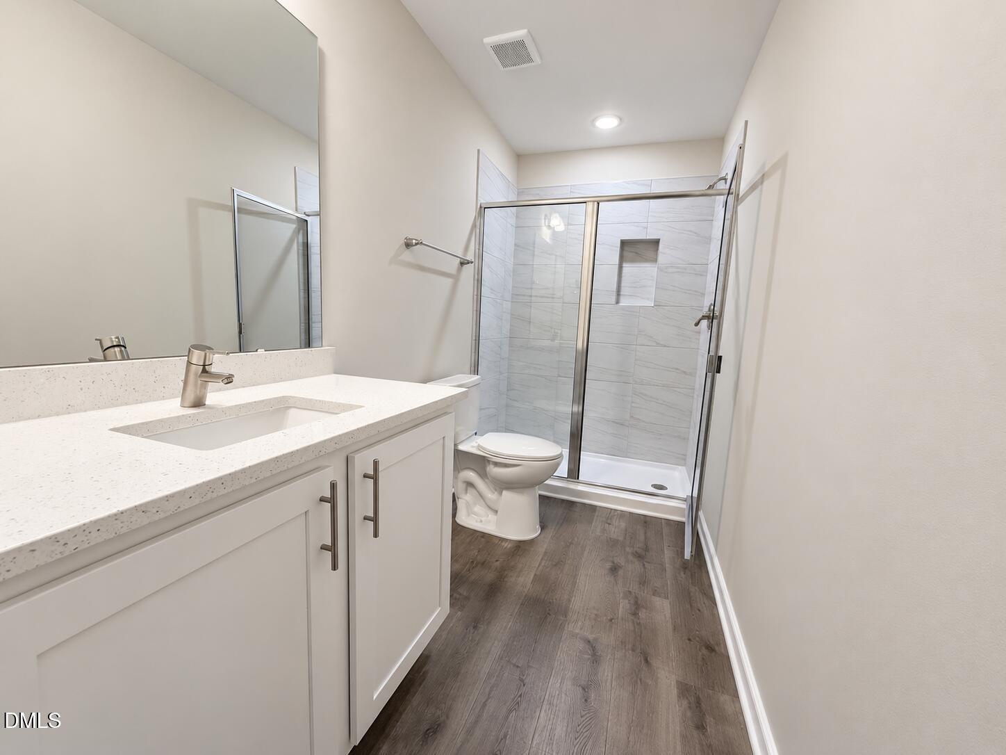 Bathroom with a white vanity, dark wood-look flooring, and a glass-enclosed tiled shower.