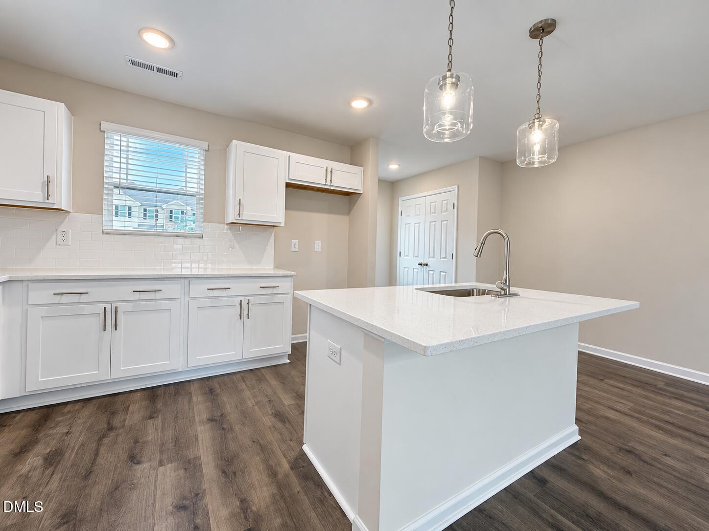Kitchen with a large white island, quartz countertop, and glass pendant lights.