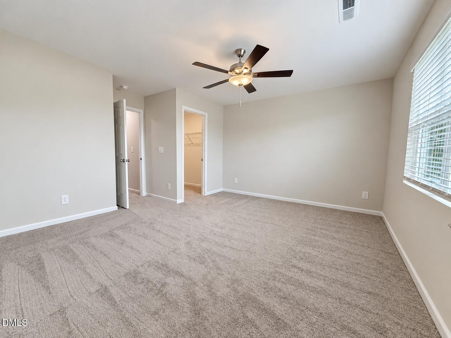 Empty carpeted bedroom with a ceiling fan, wide window with blinds, and open closet.