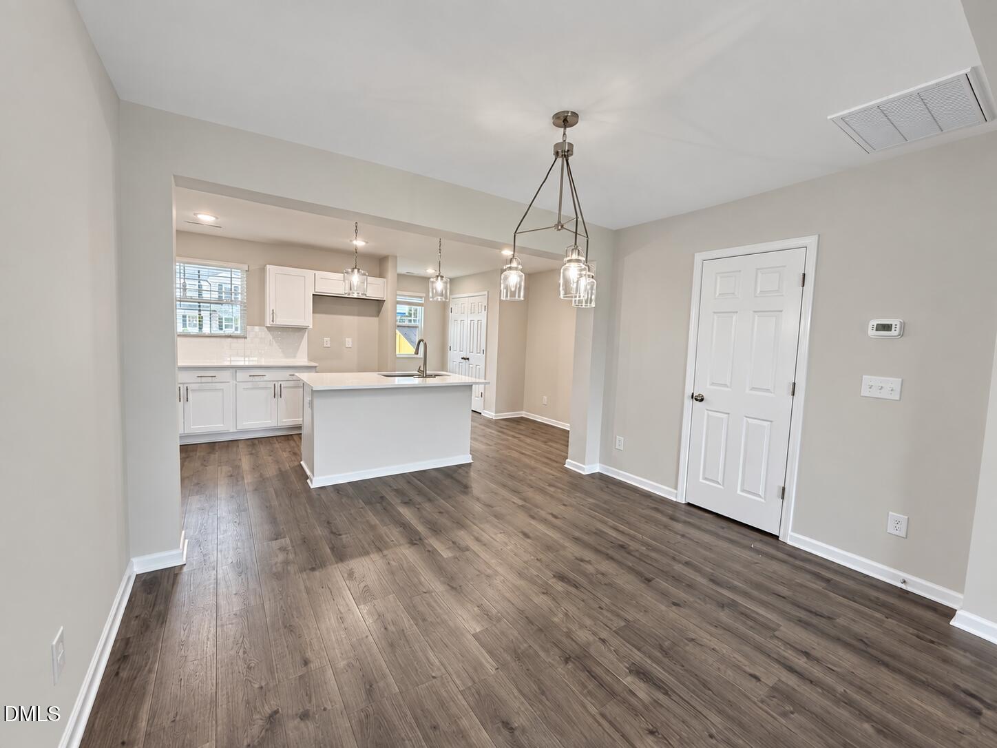 Empty dining area opening into a white kitchen with an island and pendant lights.