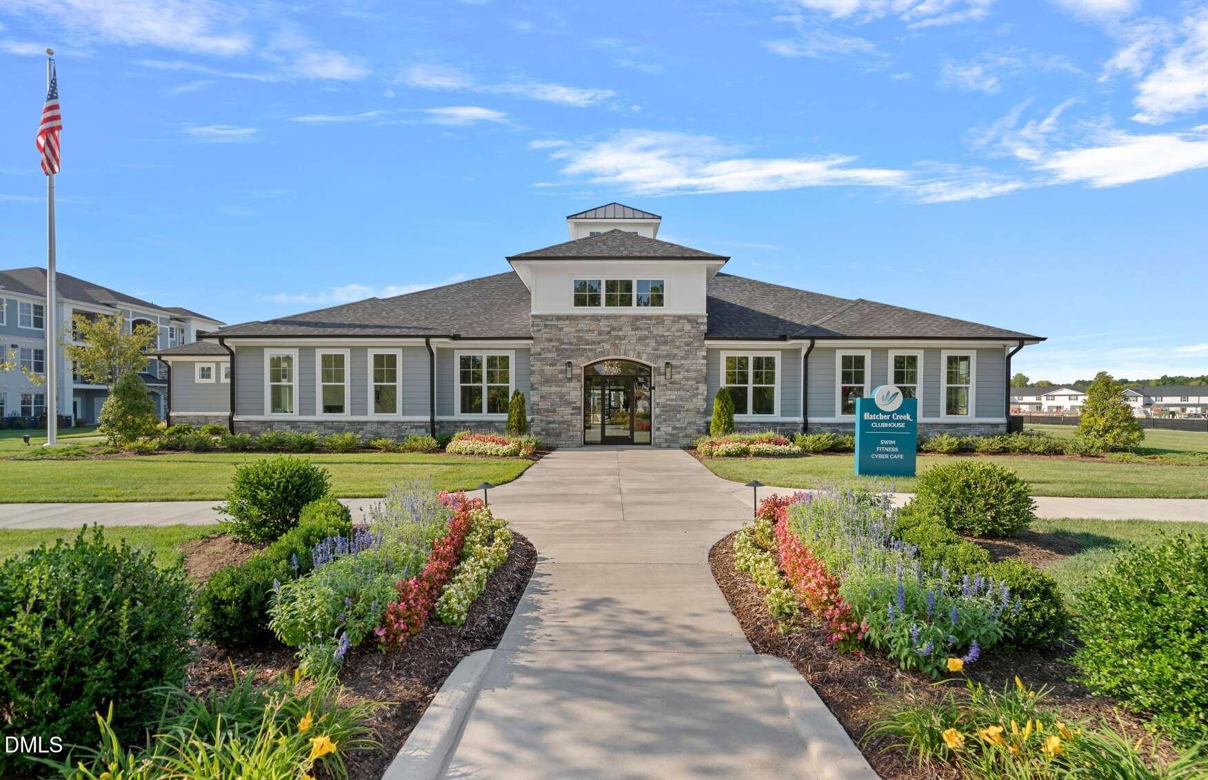 Hatcher Creek clubhouse with a stone entrance, flower beds, and a sign listing community amenities.