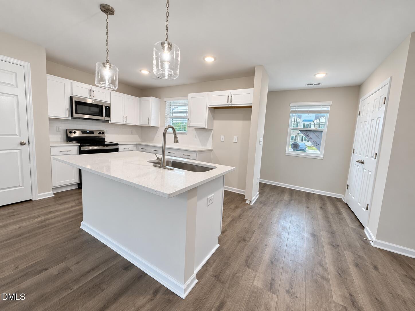 Vacant kitchen with a large white island, stainless steel appliances, and an open dining area.