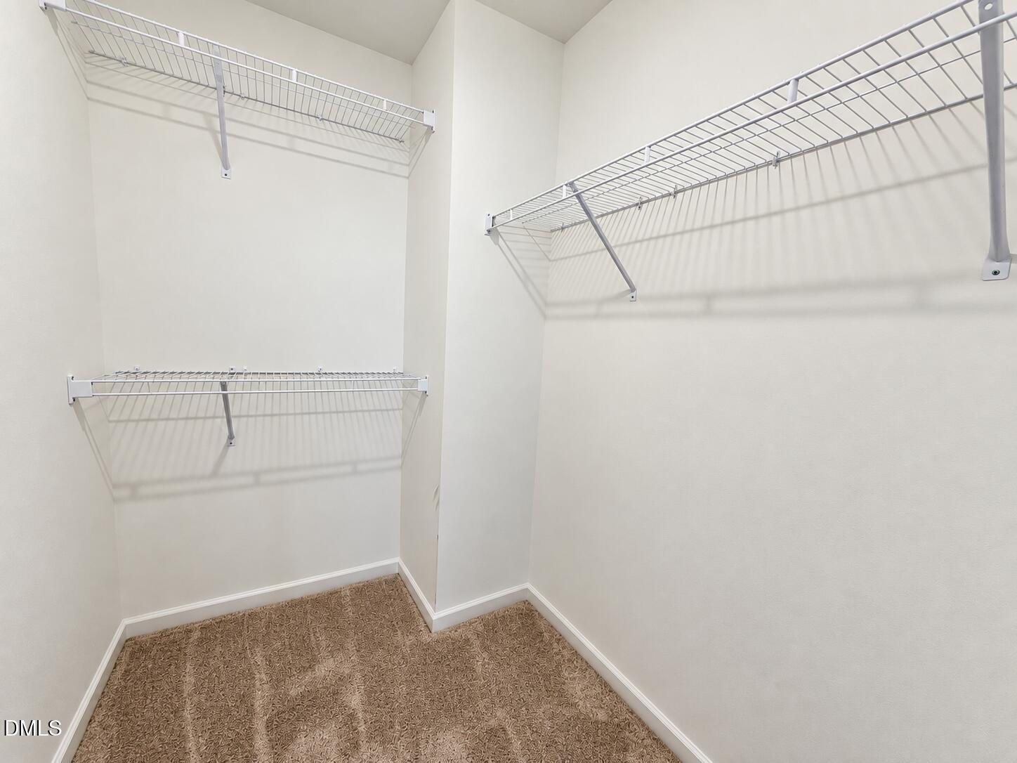Walk-in closet with wire shelving on three walls and tan carpet.