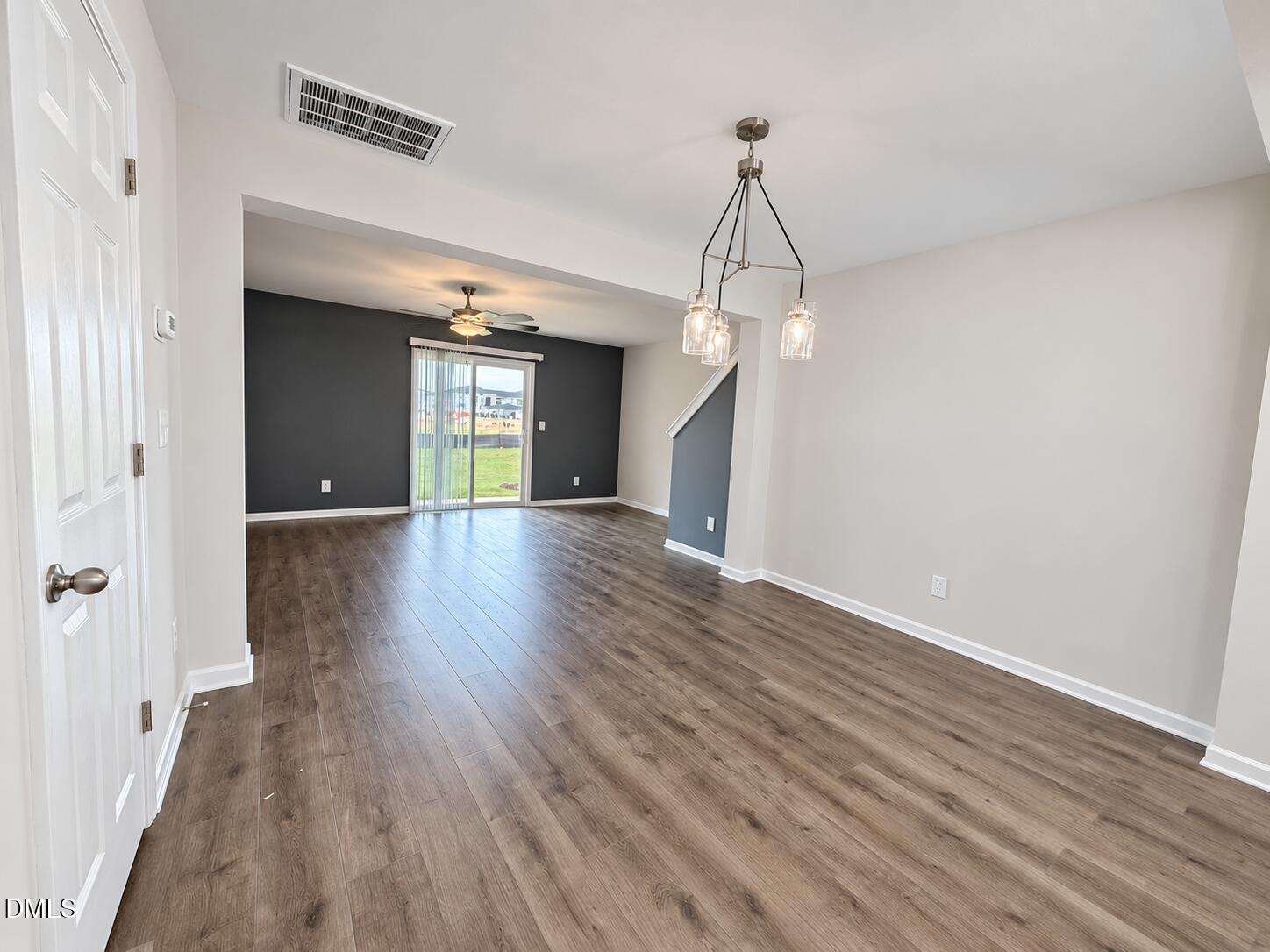 Open-plan dining and living area with wood-look floors, pendant lights, and a sliding glass door.