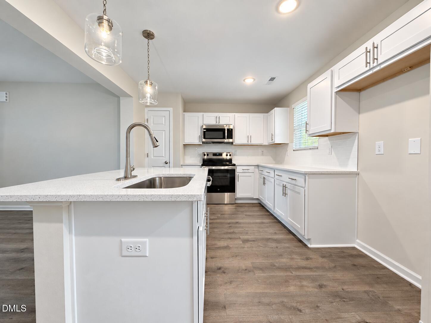 Kitchen with white cabinetry, stainless steel appliances, and a large island with a sink.