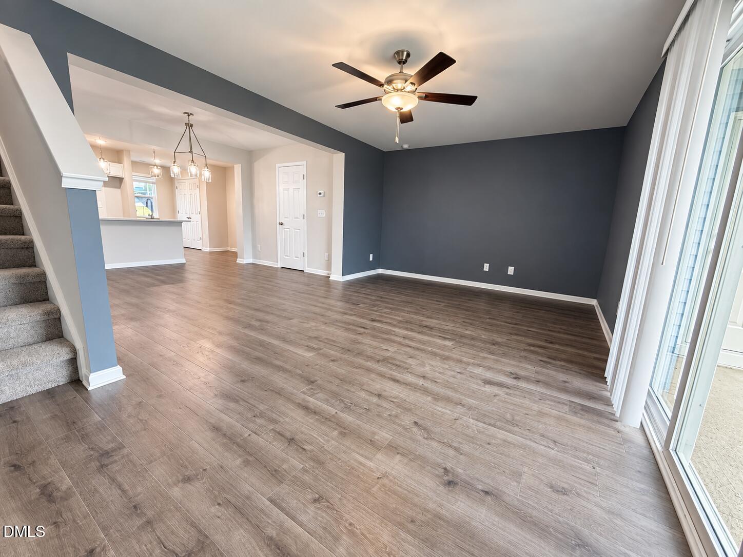 Empty living room with gray walls, wood-look floors, sliding glass doors, and an open kitchen area.