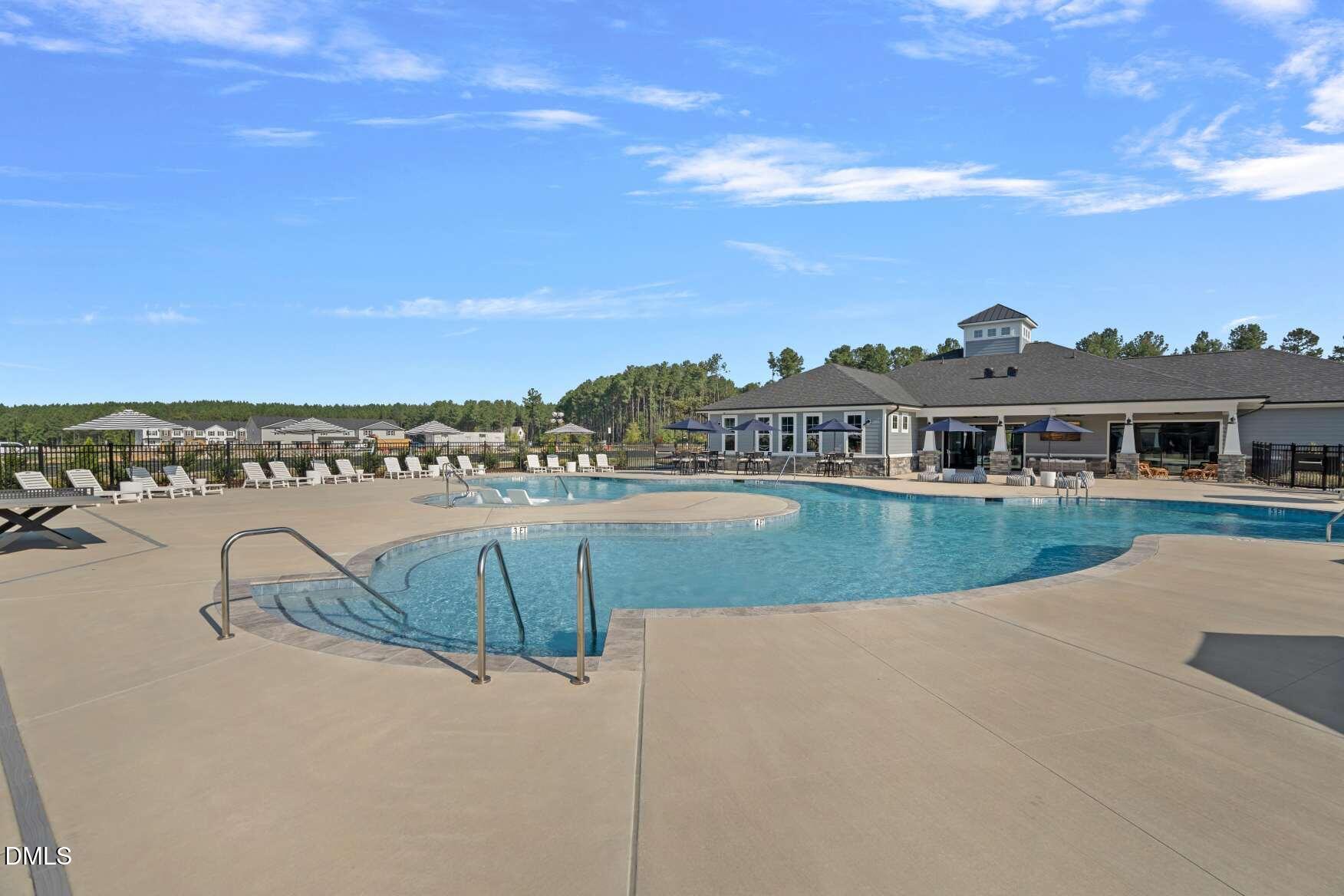 Community swimming pool with a curved shallow section, lounge chairs, umbrellas, and an adjacent clubhouse.