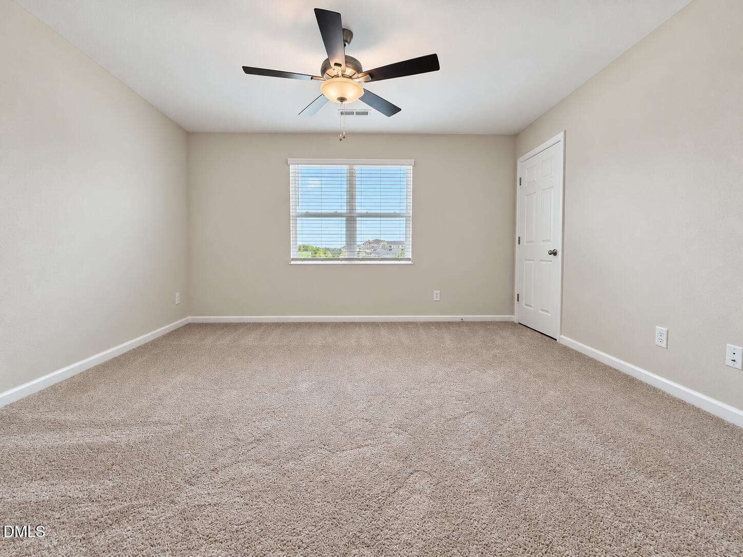 Empty carpeted bedroom with a ceiling fan, window, and closed door.
