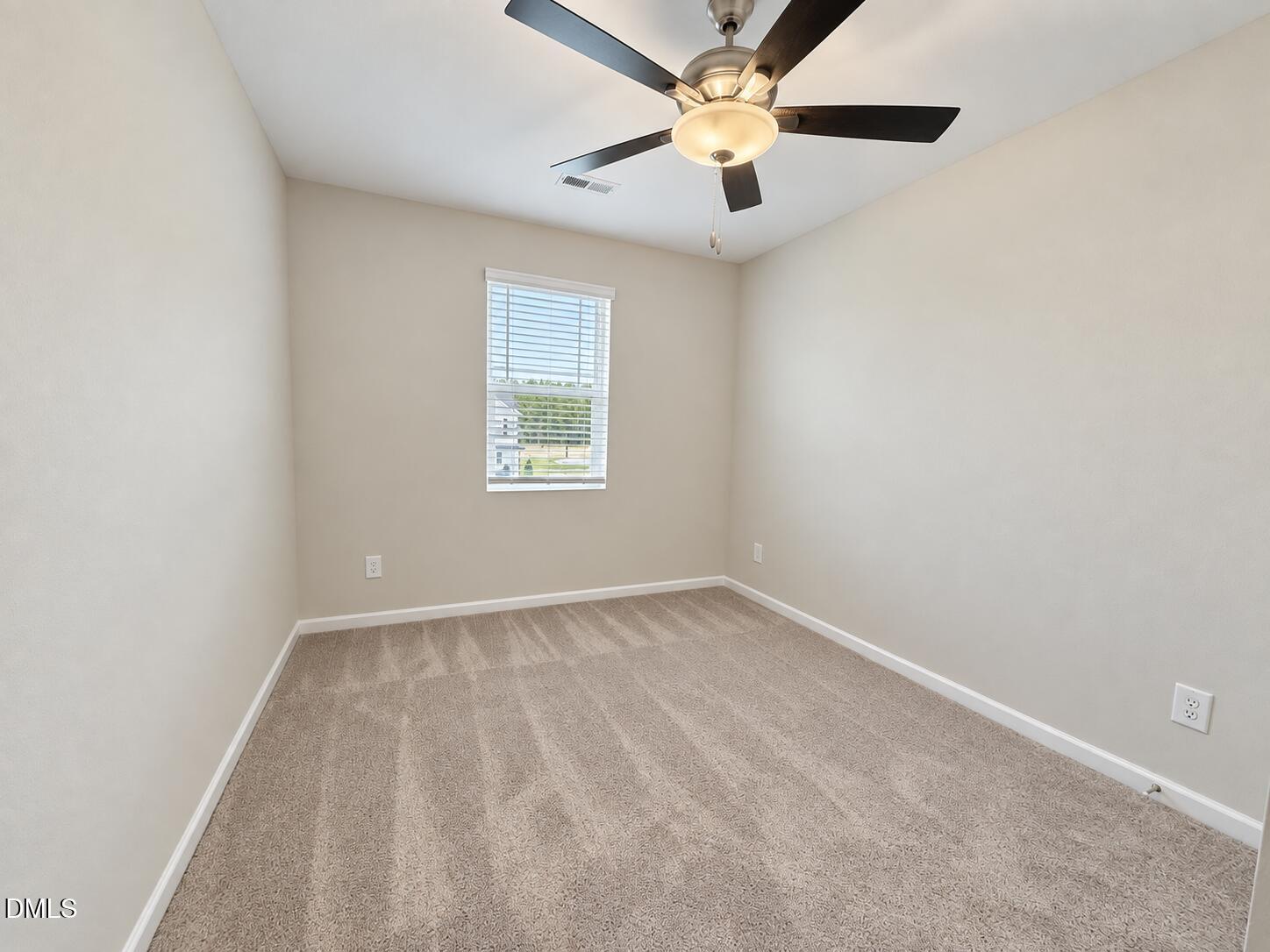 Empty bedroom with beige carpet, a window with blinds, and a ceiling fan.