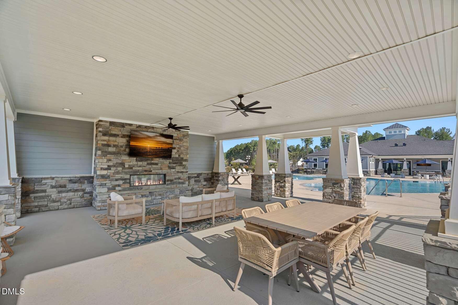 Covered patio with a stone fireplace and dining area overlooking a swimming pool.