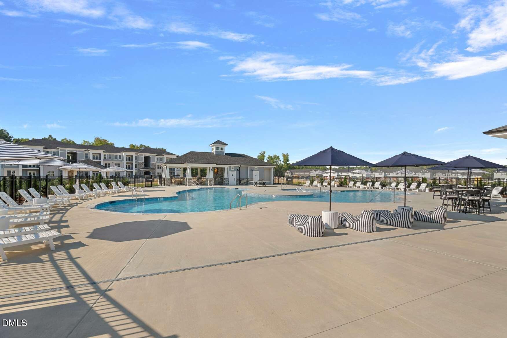Community pool with lounge chairs, striped patio seating, and umbrellas beside the clubhouse.