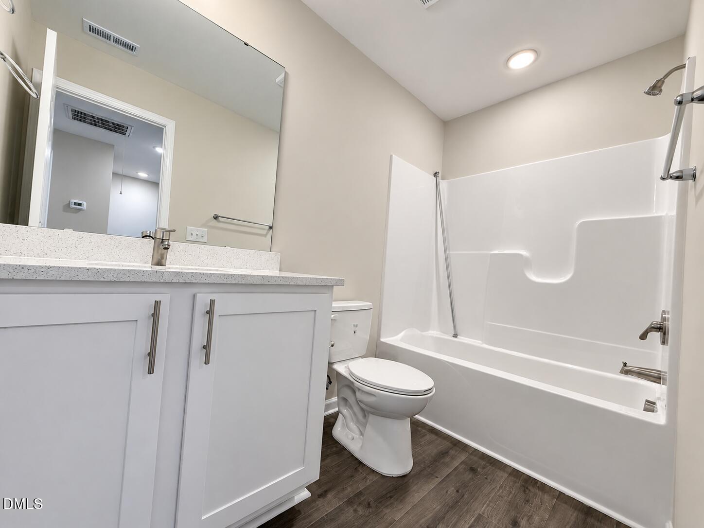Bathroom with a white vanity, tub-shower combination, toilet, and dark wood-look flooring.