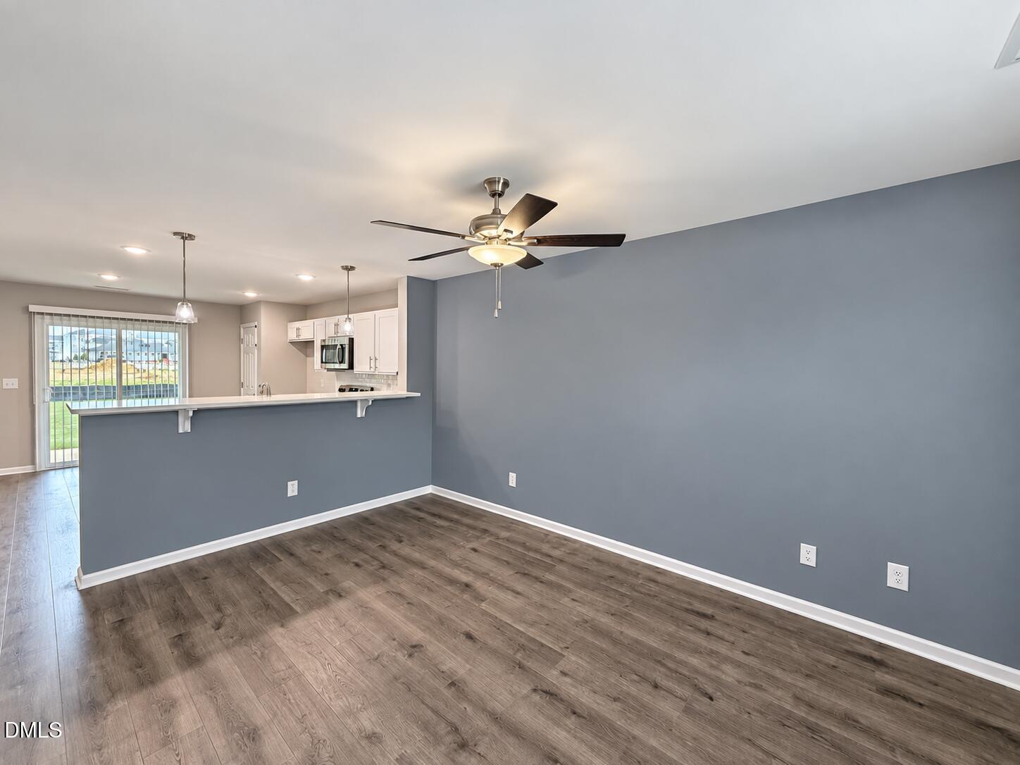 Vacant living and dining area with blue-gray walls, wood-look floors, and a ceiling fan beside the kitchen.