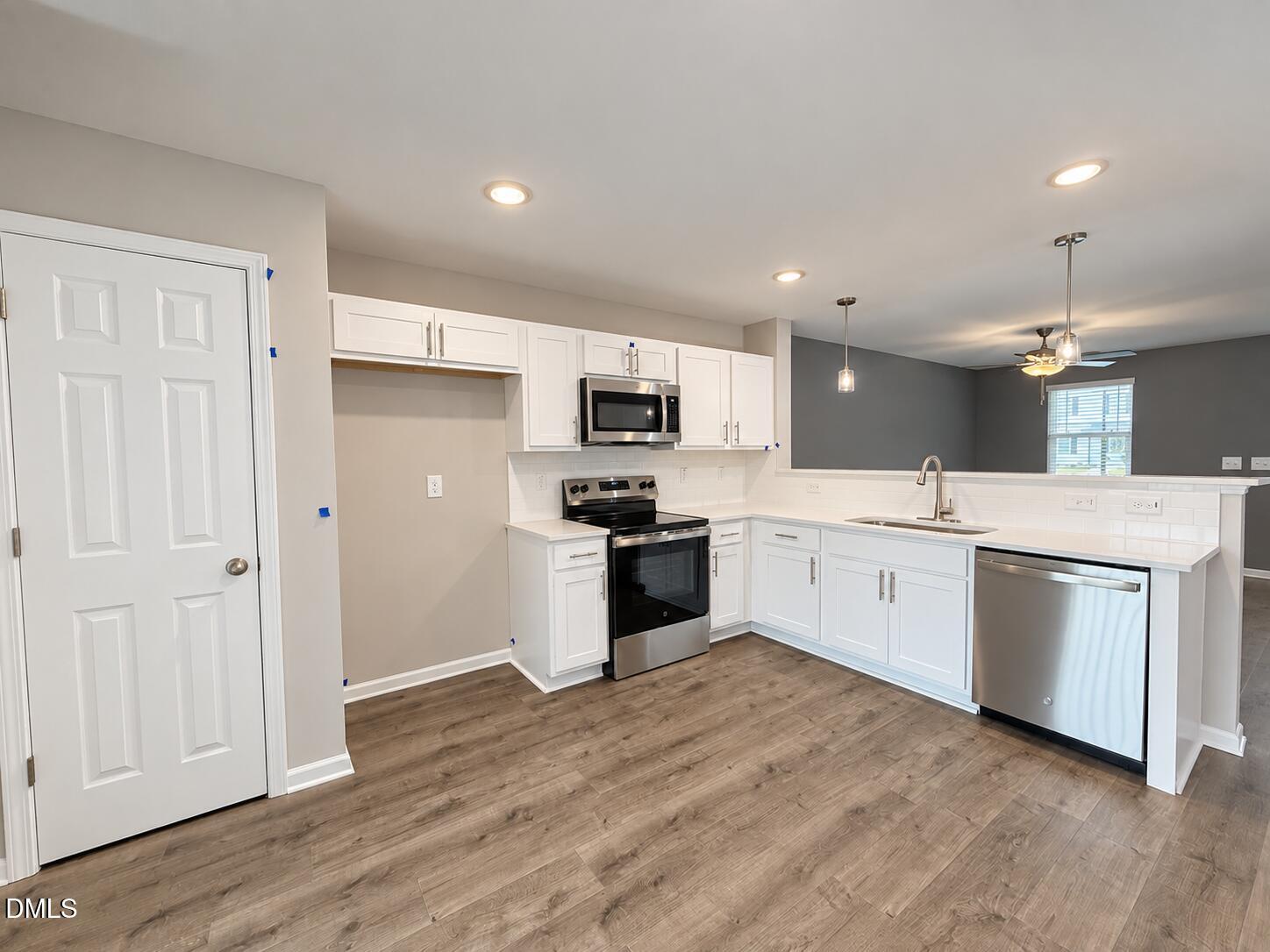 Vacant kitchen with white cabinets, stainless steel appliances, and a peninsula sink.
