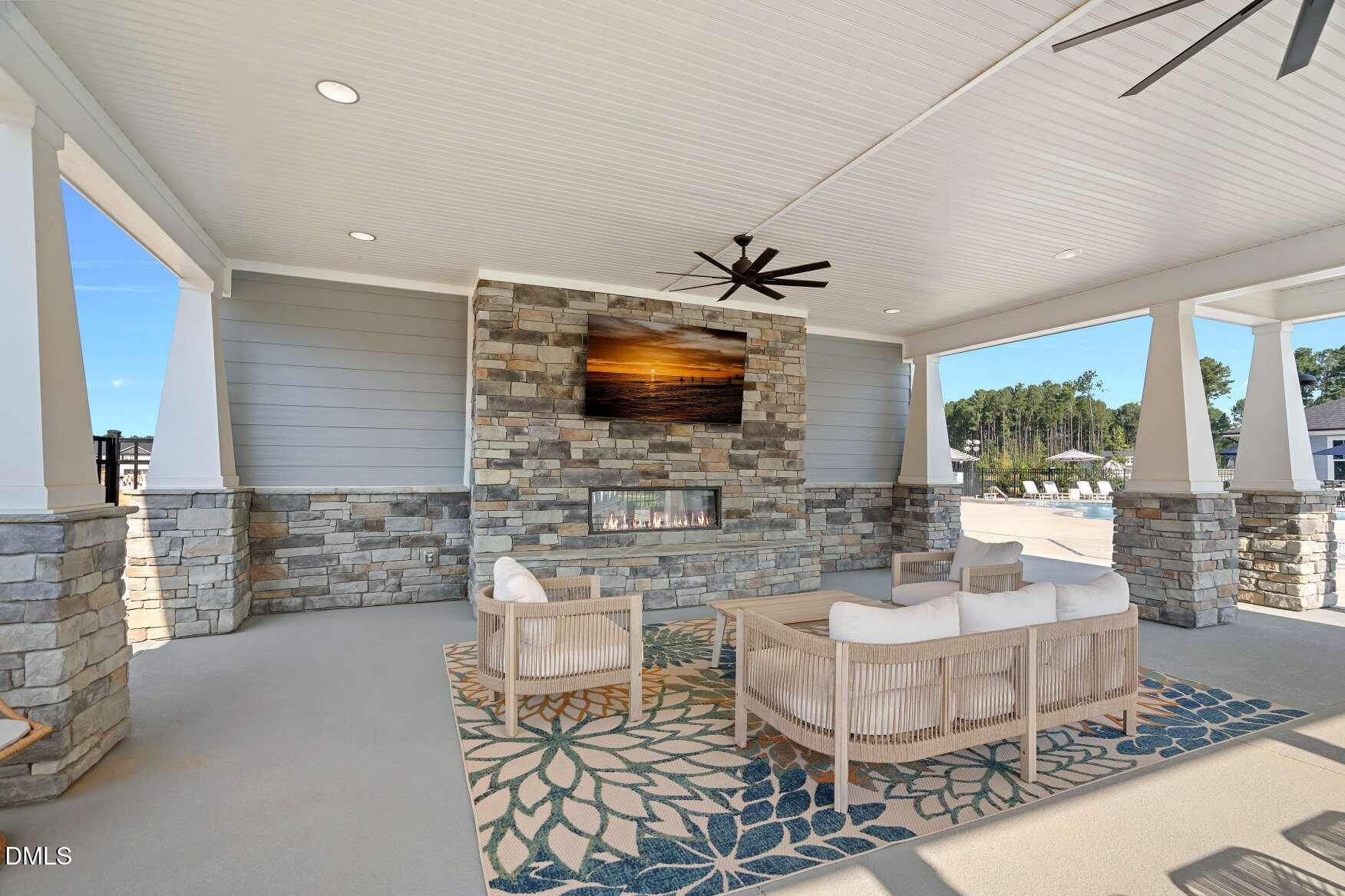 Covered patio with a stone fireplace, ceiling fan, and furnished seating area overlooking a pool.