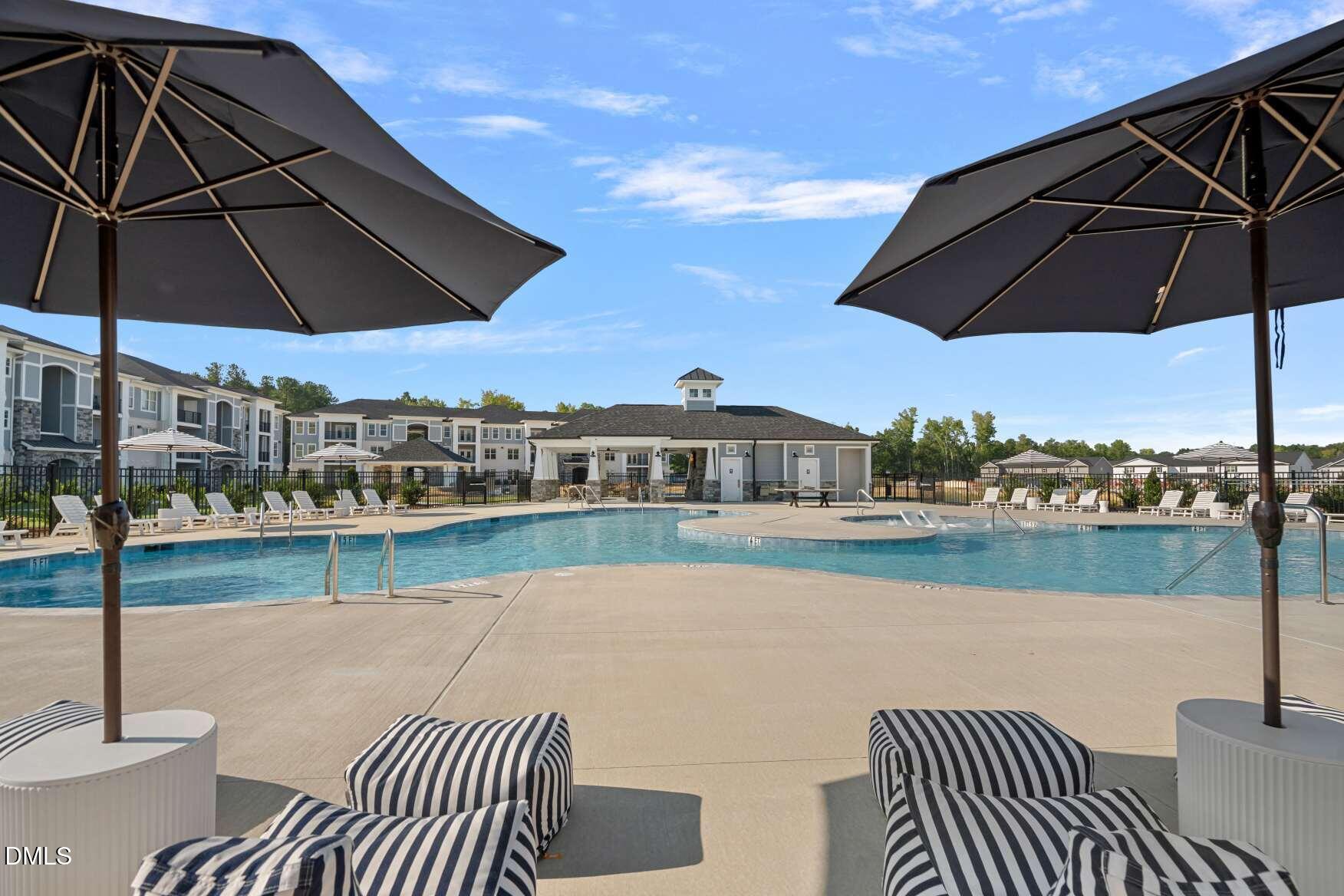 Community pool with striped lounge cushions, large umbrellas, and apartment buildings behind it.