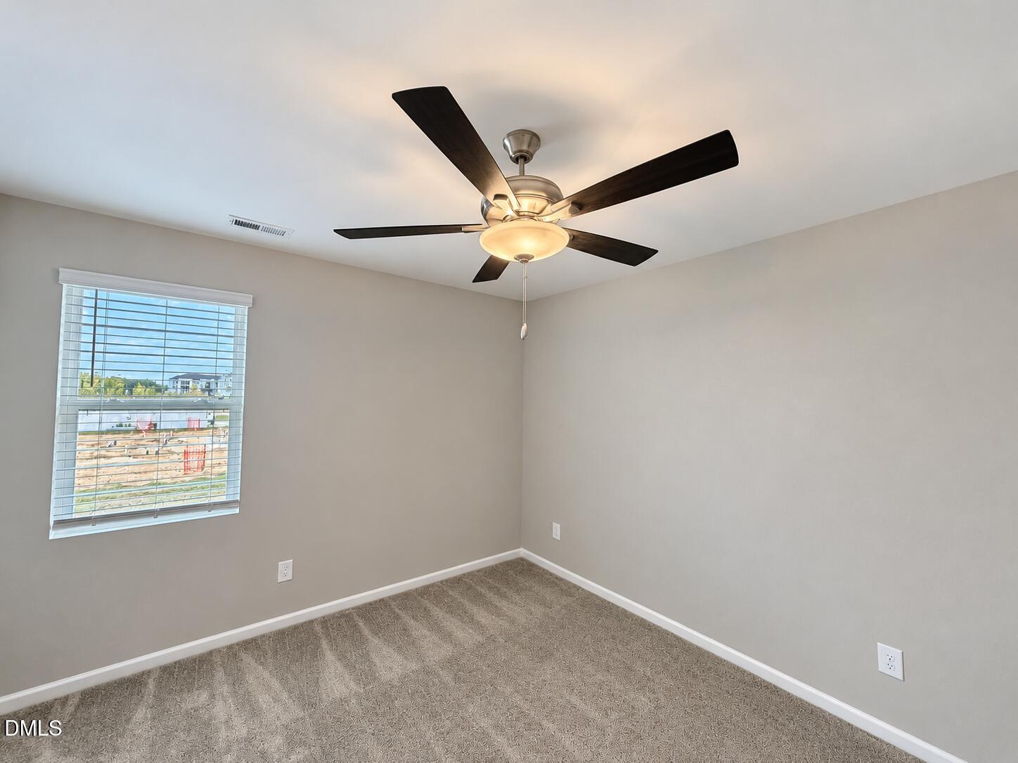 Empty carpeted bedroom with a dark-bladed ceiling fan and a window overlooking a construction site.