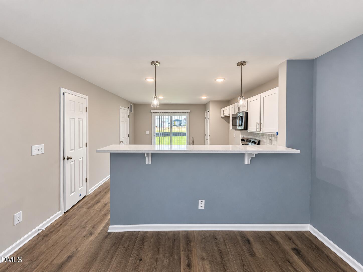 Vacant kitchen with a blue peninsula, white cabinets, stainless steel appliances, and wood-look flooring.