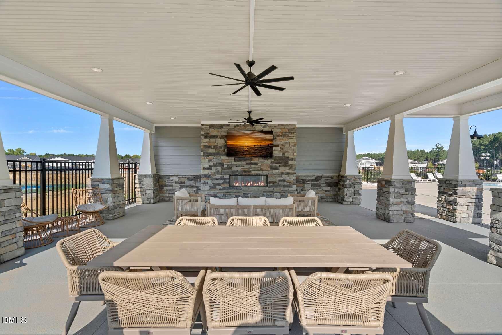 Covered outdoor pavilion with dining furniture, ceiling fans, and a stone fireplace.