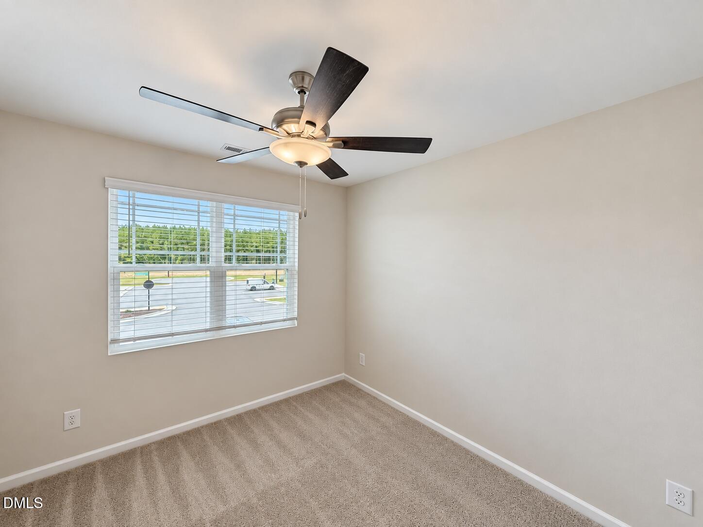 Empty carpeted room with a wide window and ceiling fan with light.