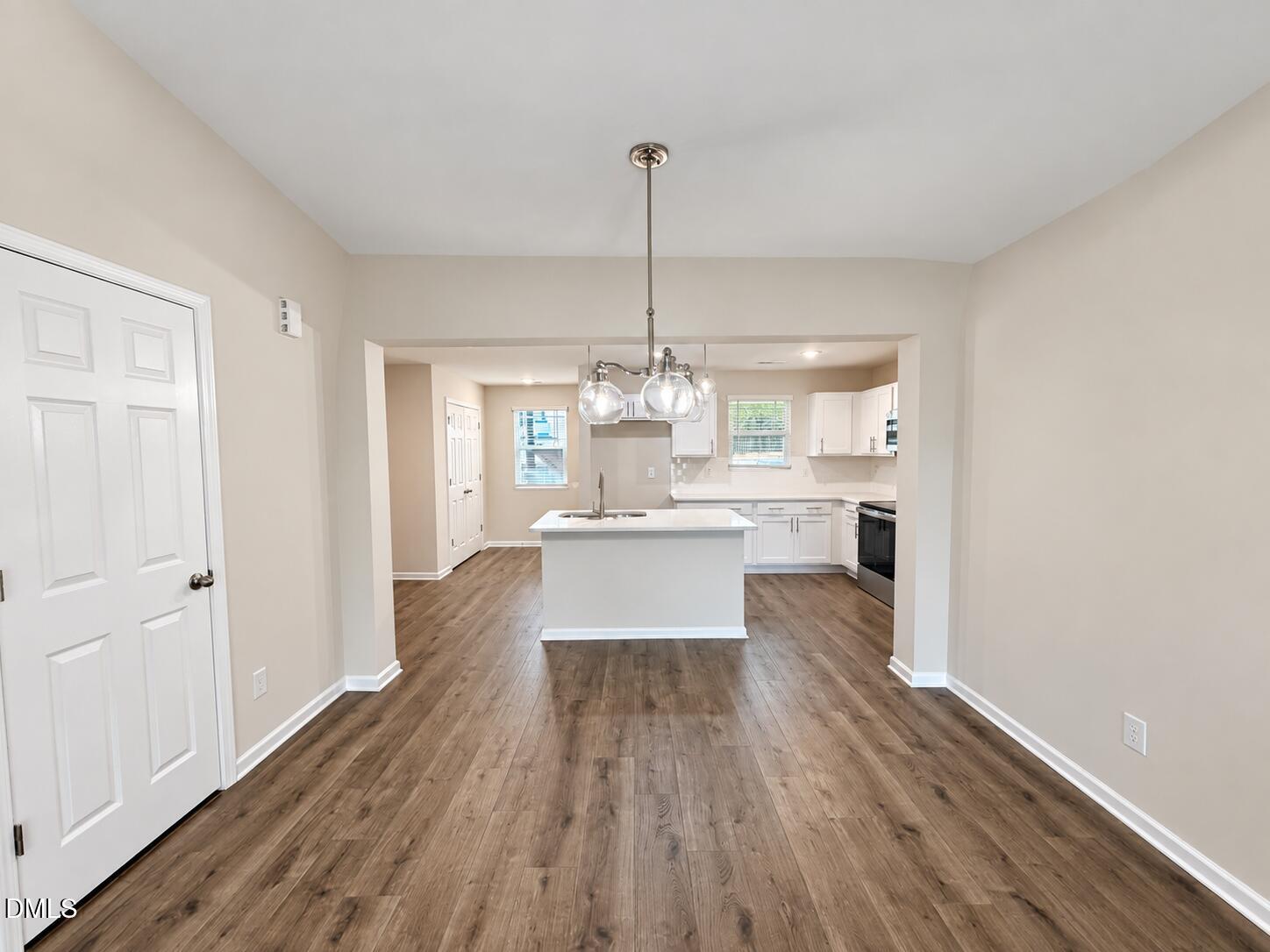 Unfurnished dining area opens into a white kitchen with an island and wood-look floors.